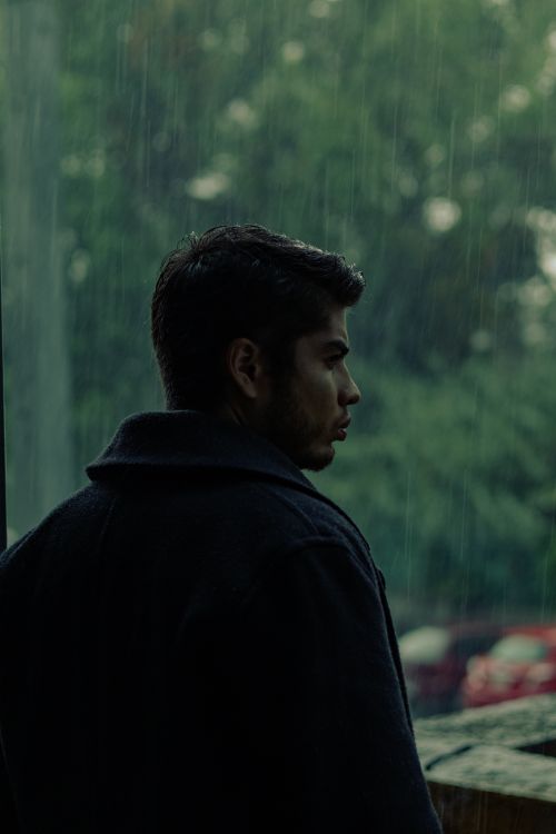 Free A man gazes out a window on a rainy day, creating a reflective mood. Stock Photo