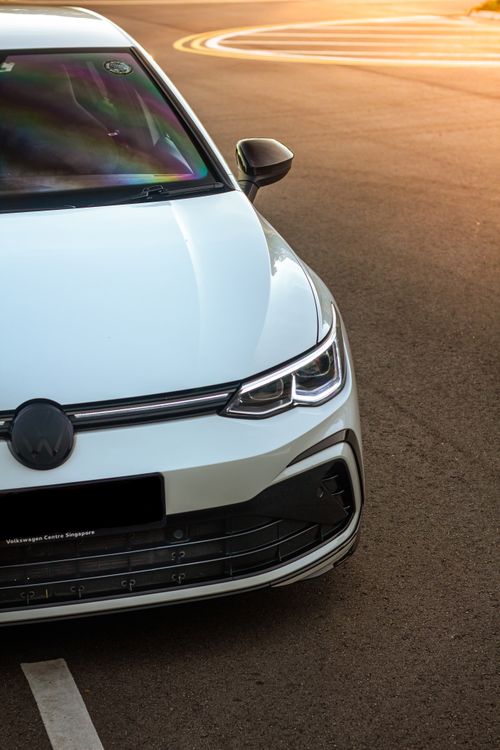 Free Close-up of a modern white car parked on asphalt at sunset, showcasing sleek design and luxury. Stock Photo