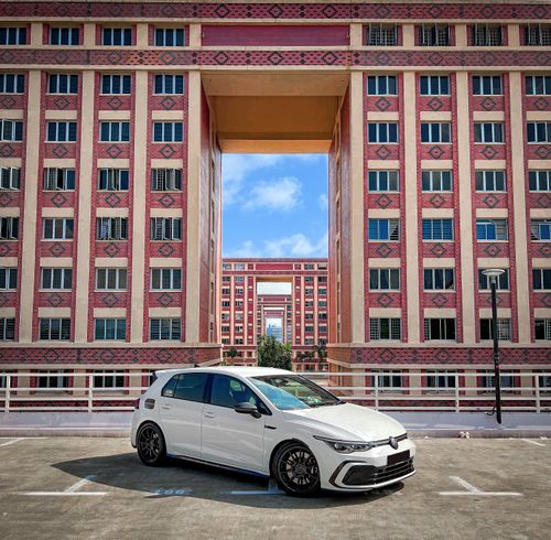 Free A sleek white car parked in front of geometric modern architecture under a clear sky. Stock Photo