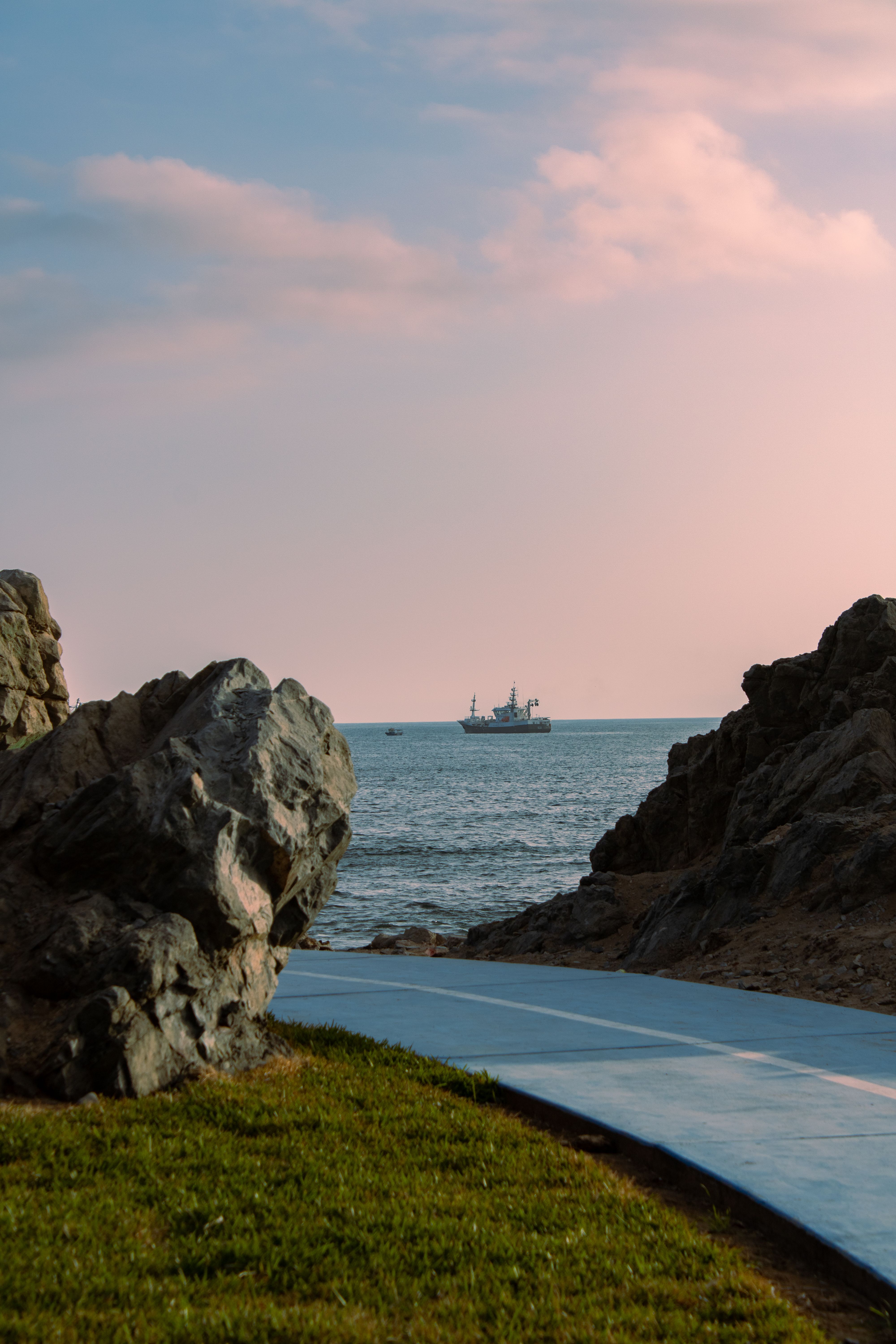 Capture of a tranquil sunset by the rocky beach path in Ilo, Perú, with a distant ship on the horizon.