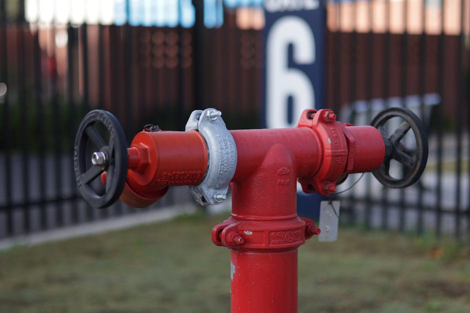 Close-up of a red industrial valve hydrant in an outdoor setting with a fence backdrop.