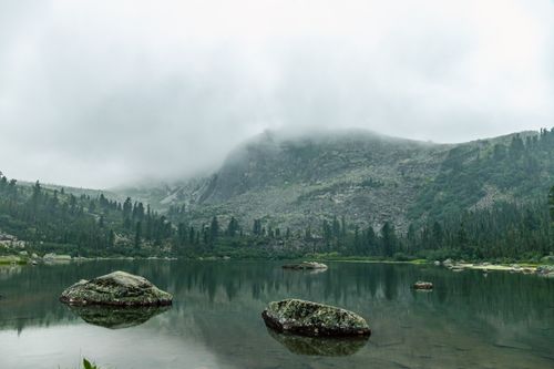 Free A serene lake surrounded by misty mountains and lush greenery, ideal for nature enthusiasts. Stock Photo
