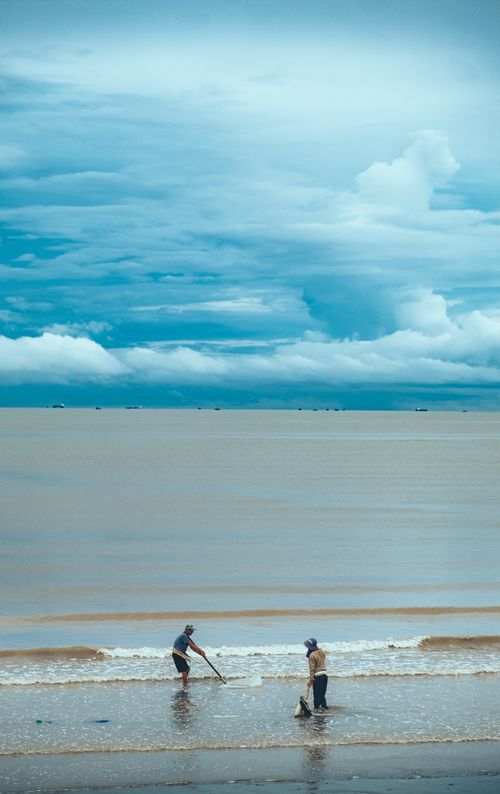Free Beachgoers enjoying a tranquil ocean view under a dramatic sky at dusk. Stock Photo