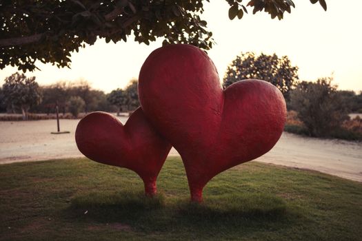 Large red heart sculptures in a tranquil park setting during sunset evoke romance and serenity.