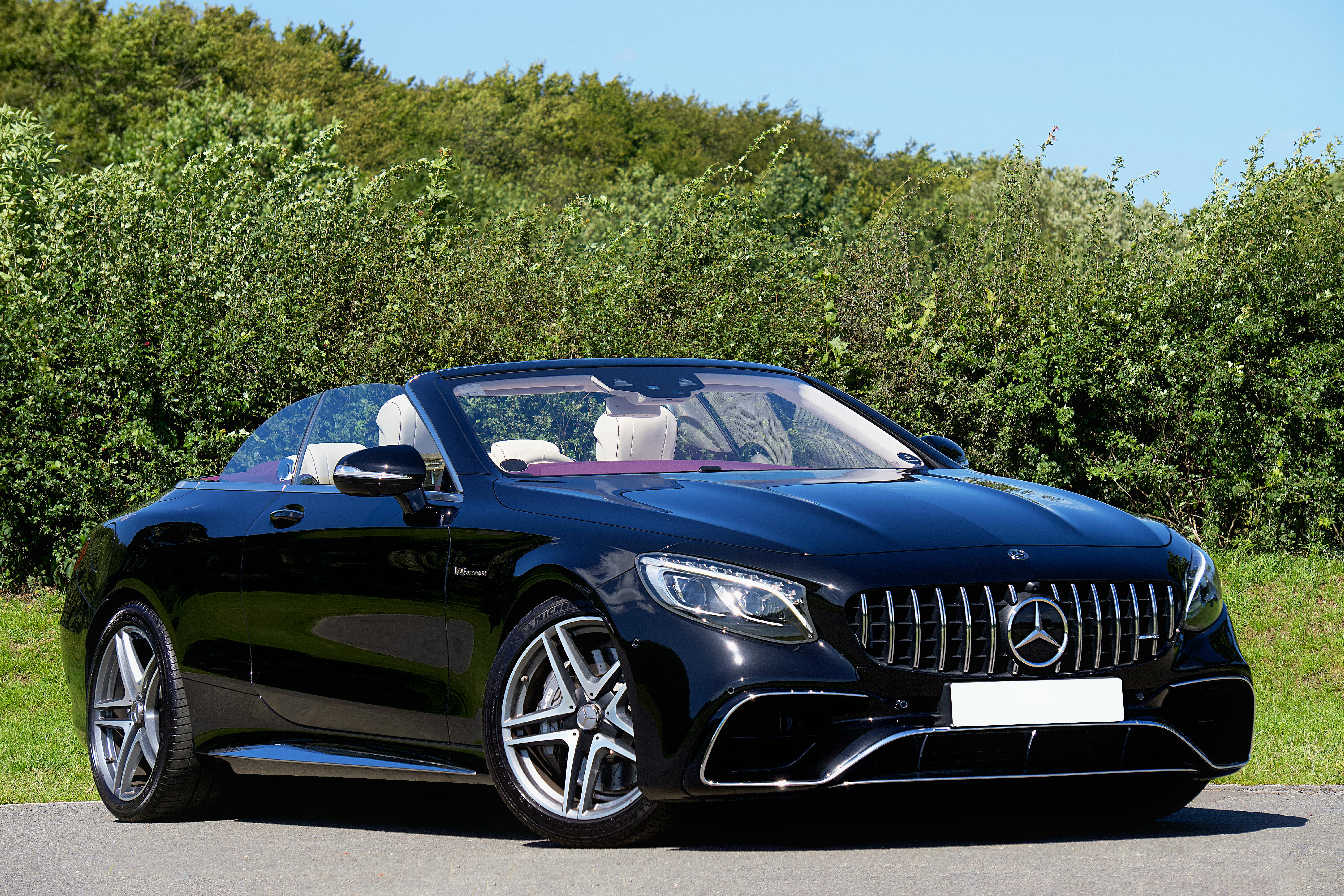 Elegant black convertible parked on a scenic road against green foliage, showcasing luxury and style.