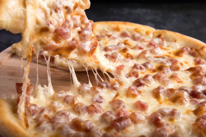Kousek sýrové pizzy se táhnoucím roztaveným sýrem