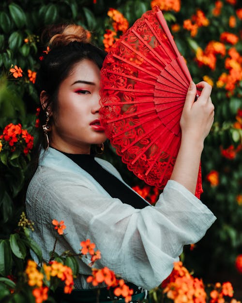 Free Woman Holding Red Fan Beside Plant With Flowers Stock Photo