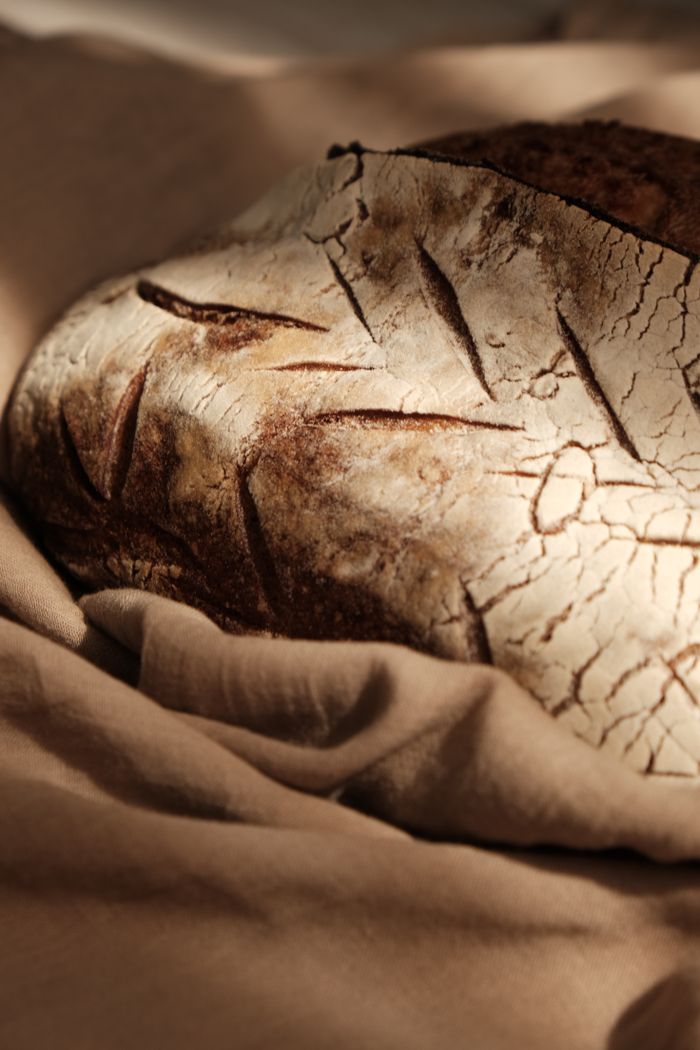 Round sourdough loaf with a scored, crackled crust resting on linen. Photo by Khadijah Karaca on Pexels