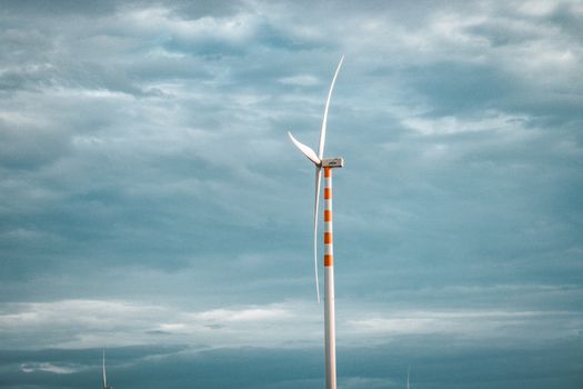 A single wind turbine stands tall against a backdrop of cloudy skies, symbolizing renewable energy.