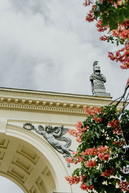 Free A captivating view of a historic arch with a statue in Munich, framed by vibrant flowers. Stock Photo