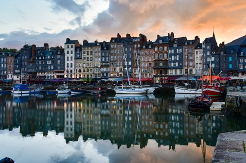 Free Colorful historic buildings and boats reflecting on the calm waters of Honfleur's harbor during sunset in Normandy, France. Stock Photo