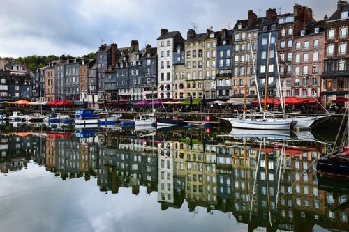 Free Charming view of Honfleur harbor with colorful buildings and boats reflecting in the water. Stock Photo