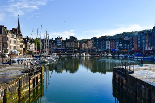 Free Charming view of Honfleur's historic harbor with boats reflecting on the water on a sunny day. Stock Photo