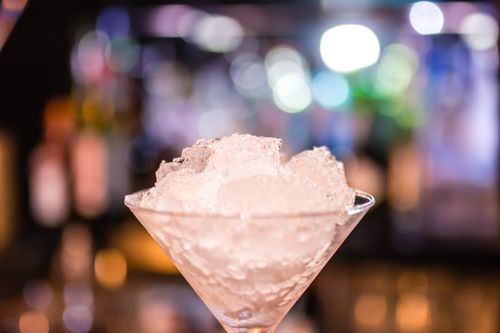 Free Elegant cocktail glass filled with crushed ice, highlighted by colorful bokeh lights in a nightclub setting. Stock Photo