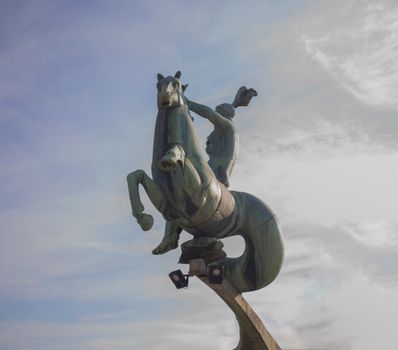 Outdoor bronze statue of a horse and rider under a cloudy sky, showcasing movement and heritage.