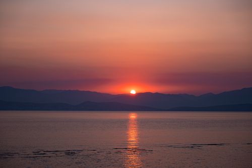 Free Serene sunset reflecting over the sea with distant mountains in Corfu, Greece. Stock Photo