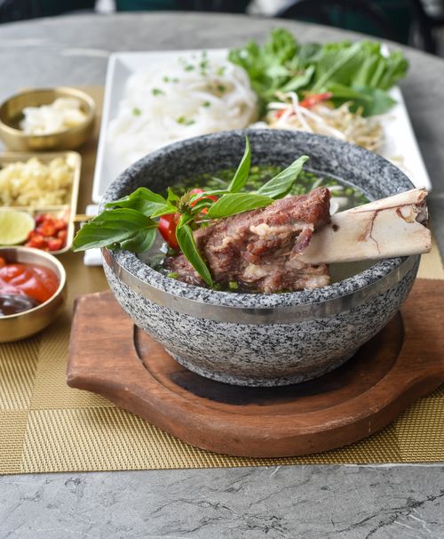 Free A flavorful bowl of beef noodle soup garnished with fresh herbs, served with side dishes. Stock Photo