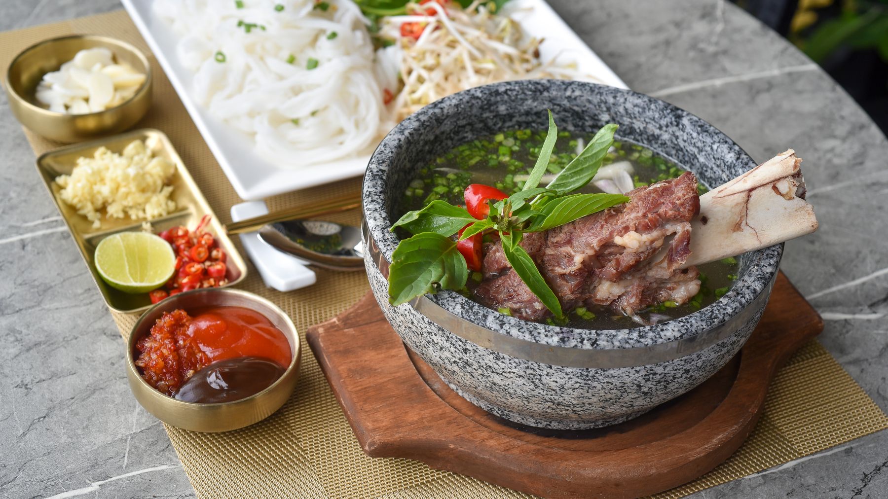 A delicious bowl of Vietnamese pho with beef and fresh garnishes served on a stone table.