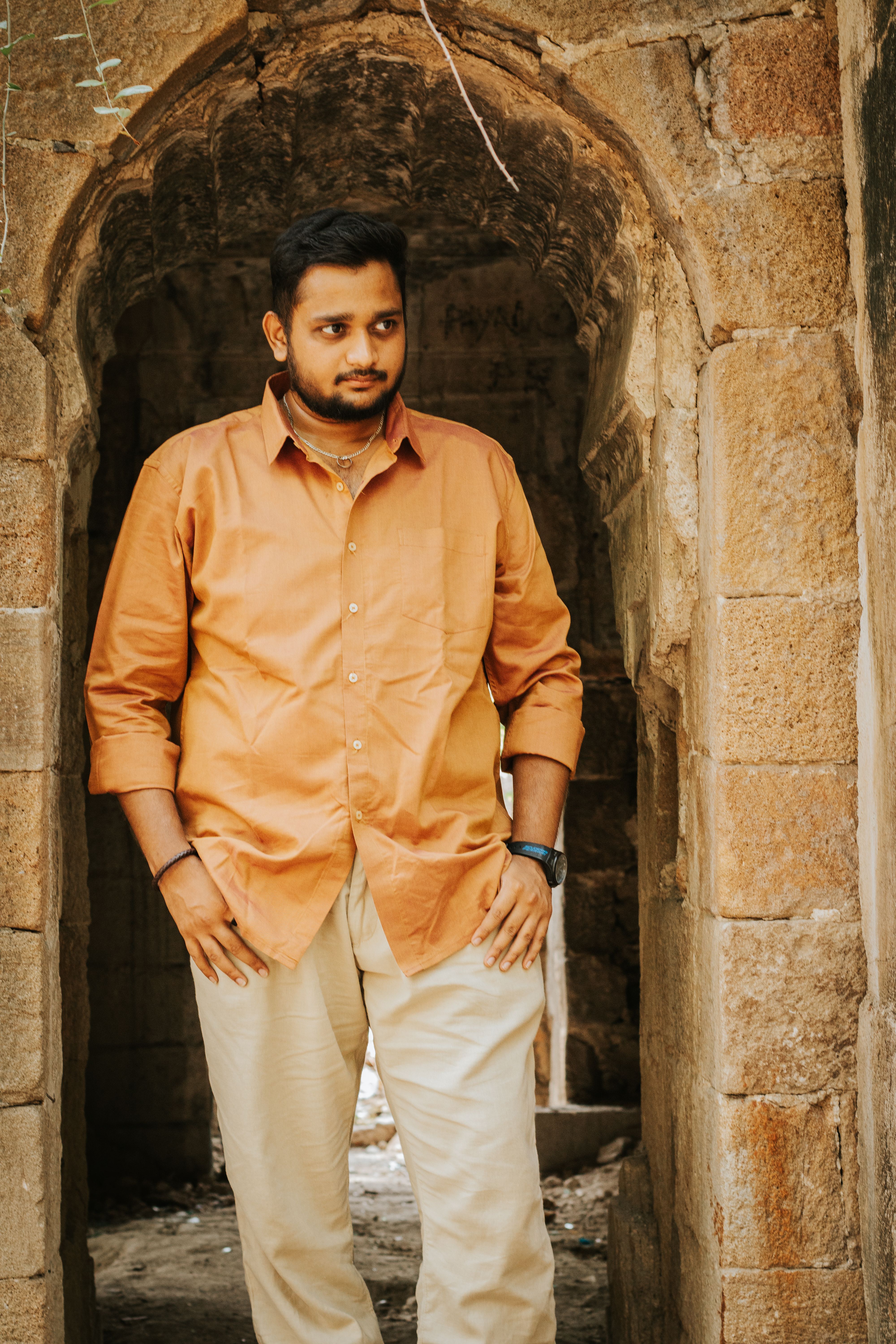 Man posing confidently in a stone archway with light clothing.