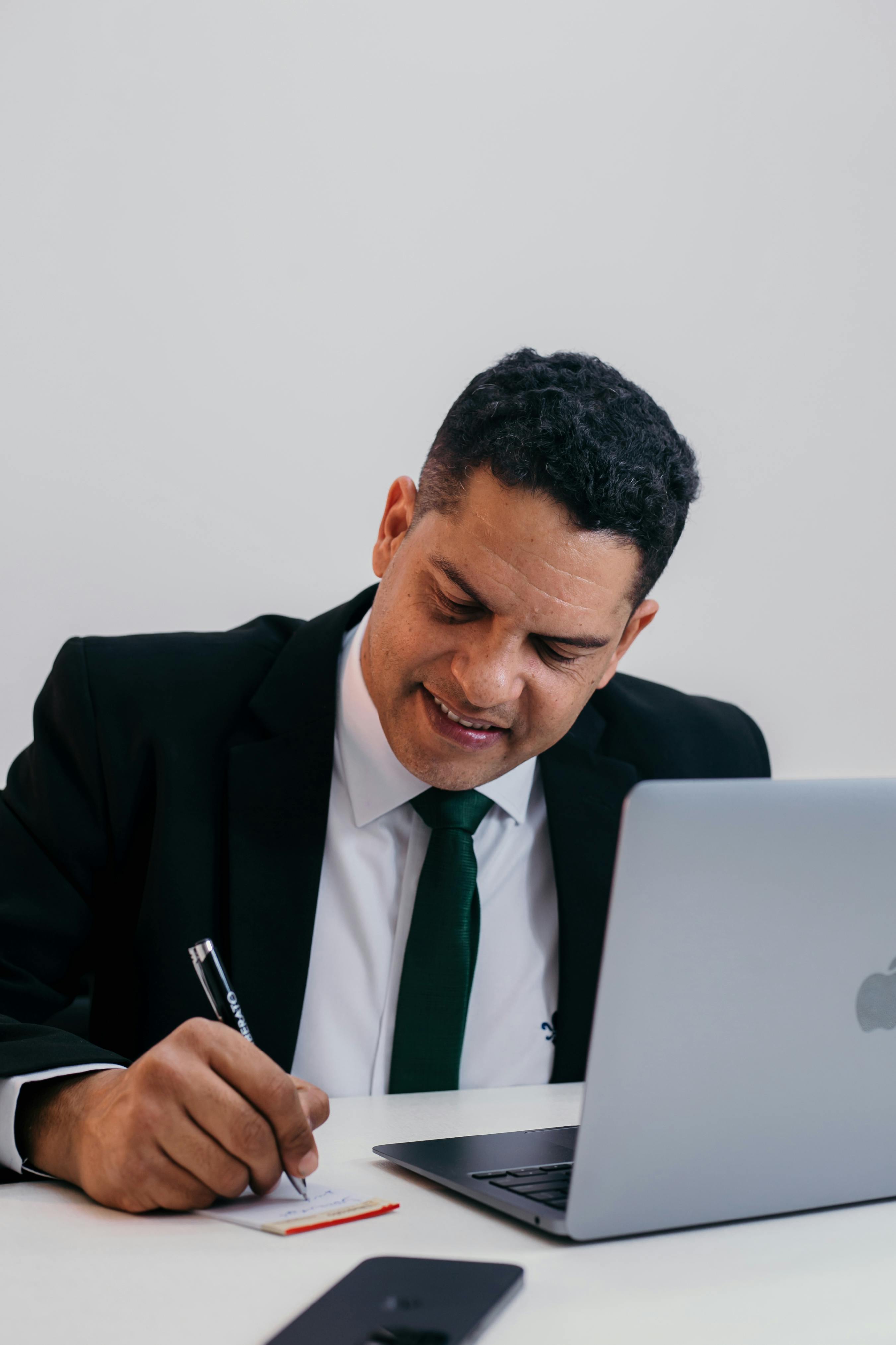 man in suit writing and working on laptop