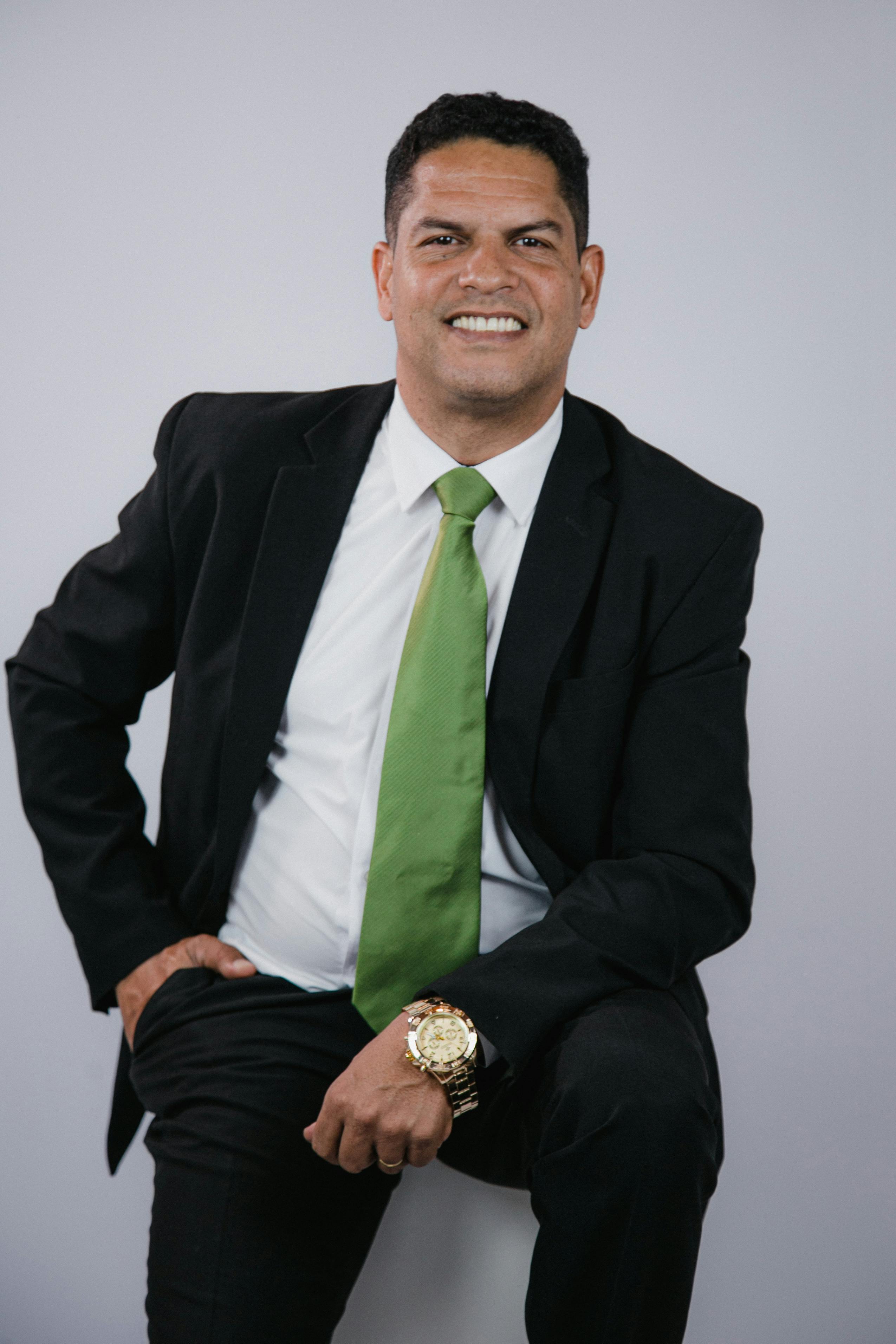 Portrait of a confident businessman in a black suit and green tie, smiling warmly.