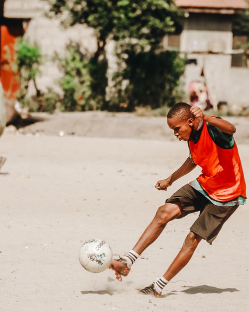 Free Boy kicking soccer ball on sandy field, showcasing energy and sportsmanship outdoors. Stock Photo