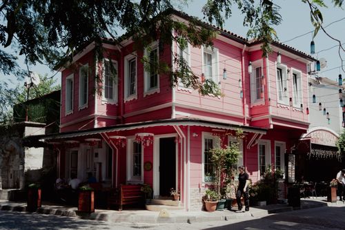 Free Vibrant pink house in an urban area with lush greenery and people enjoying the street view. Stock Photo