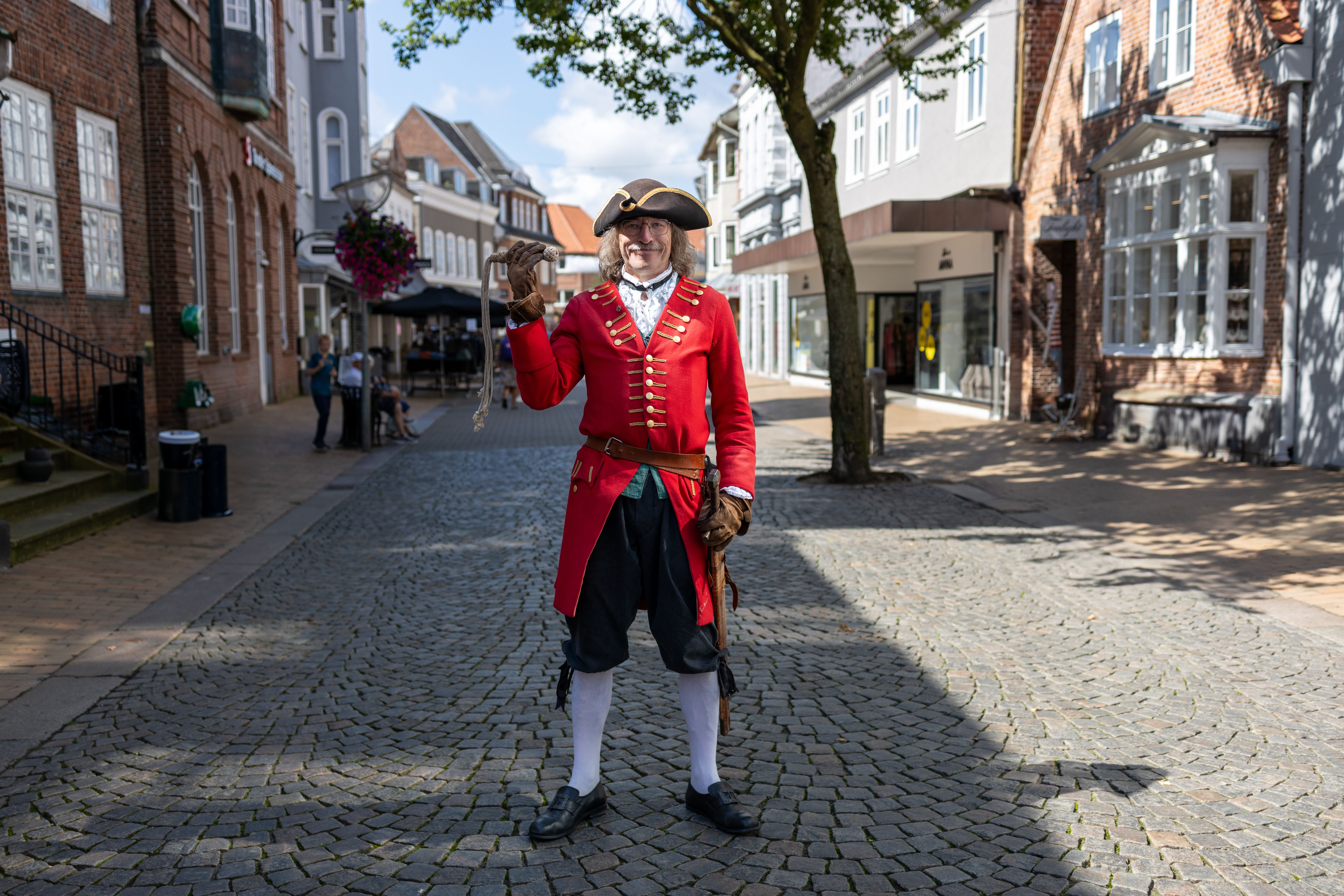 A historical reenactor in period costume poses in a charming Tondern street, Denmark.