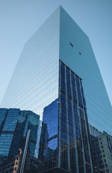 Tall modern skyscraper reflecting urban surrounding buildings under a clear sky.