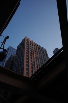 A modern skyscraper captured from below with an overpass frame against a clear sky.