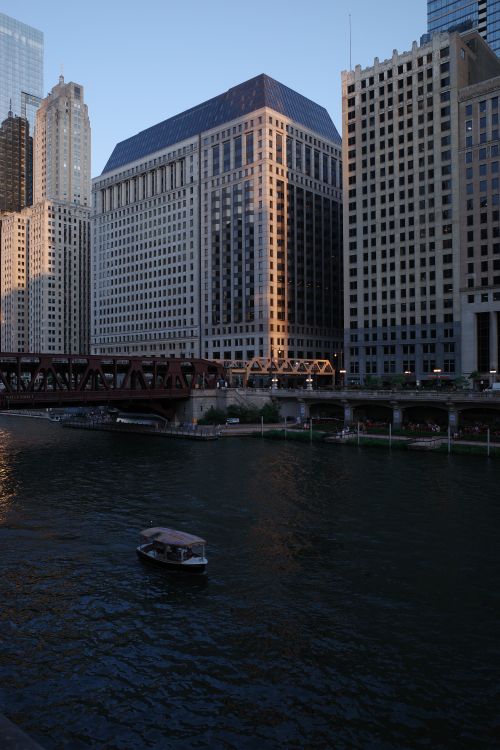 Free A cityscape view of Chicago's riverfront with towering skyscrapers and a lone boat at dusk. Stock Photo