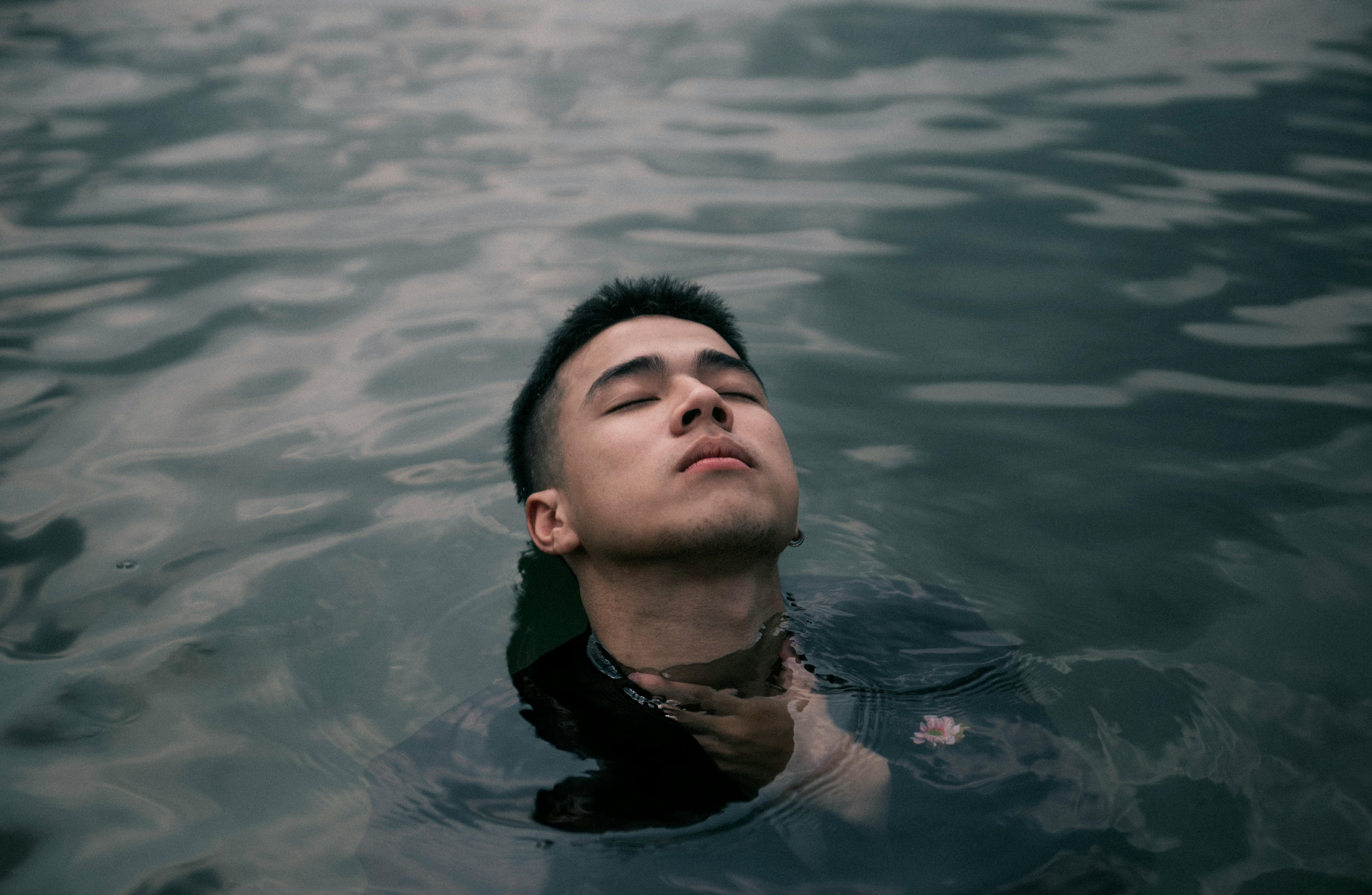 A serene portrait of an Asian man enjoying a leisurely swim in calm water, reflecting tranquility.