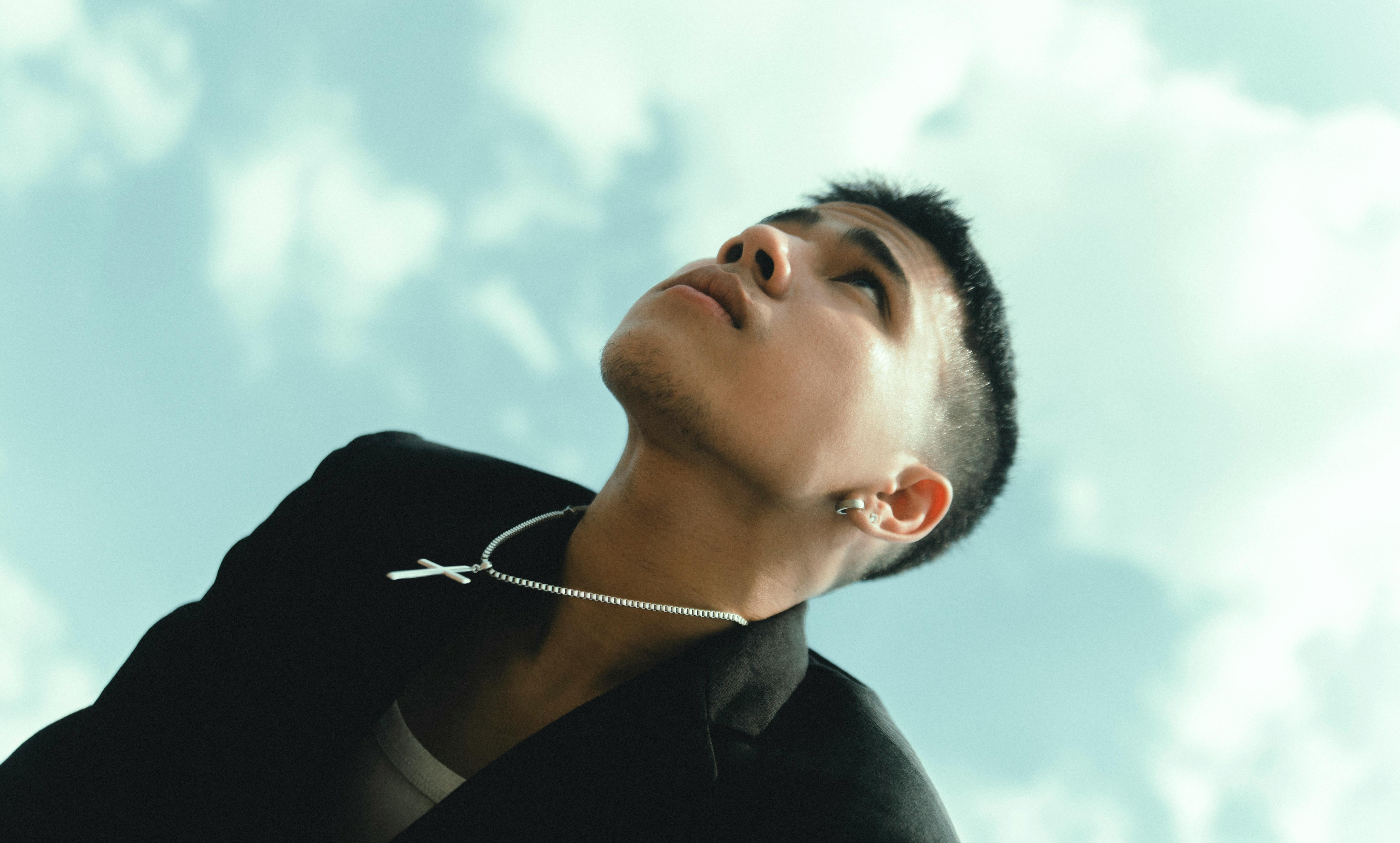 Portrait of a young Asian man gazing upwards against a bright sky, exuding a pensive mood.