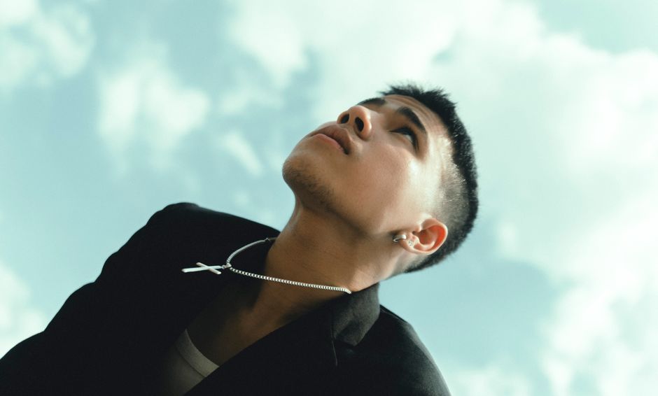 Portrait of a young Asian man gazing upwards against a bright sky, exuding a pensive mood.