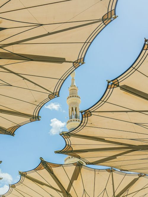 Free View of a mosque minaret through modern architectural structures against a clear blue sky. Stock Photo