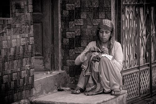 Free A thoughtful black and white portrait of a woman sewing on a stone step in an urban setting. Stock Photo