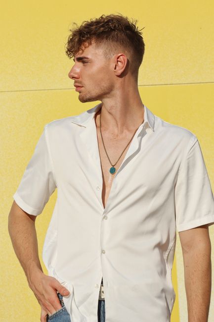 Stylish young man in white shirt posing against a vibrant yellow background.