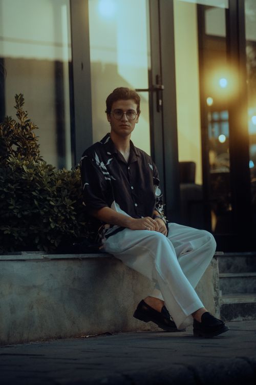 Free Portrait of a young man sitting outdoors at twilight, exuding a stylish vibe with modern fashion. Stock Photo