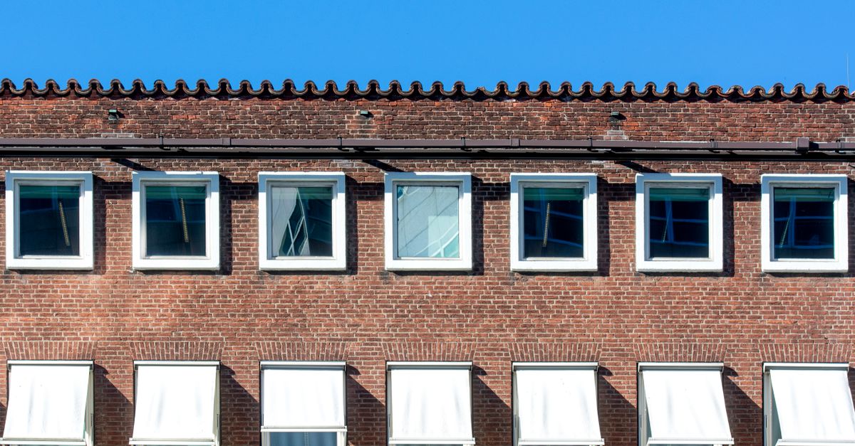 A modern brick building facade with open windows under a clear blue sky.