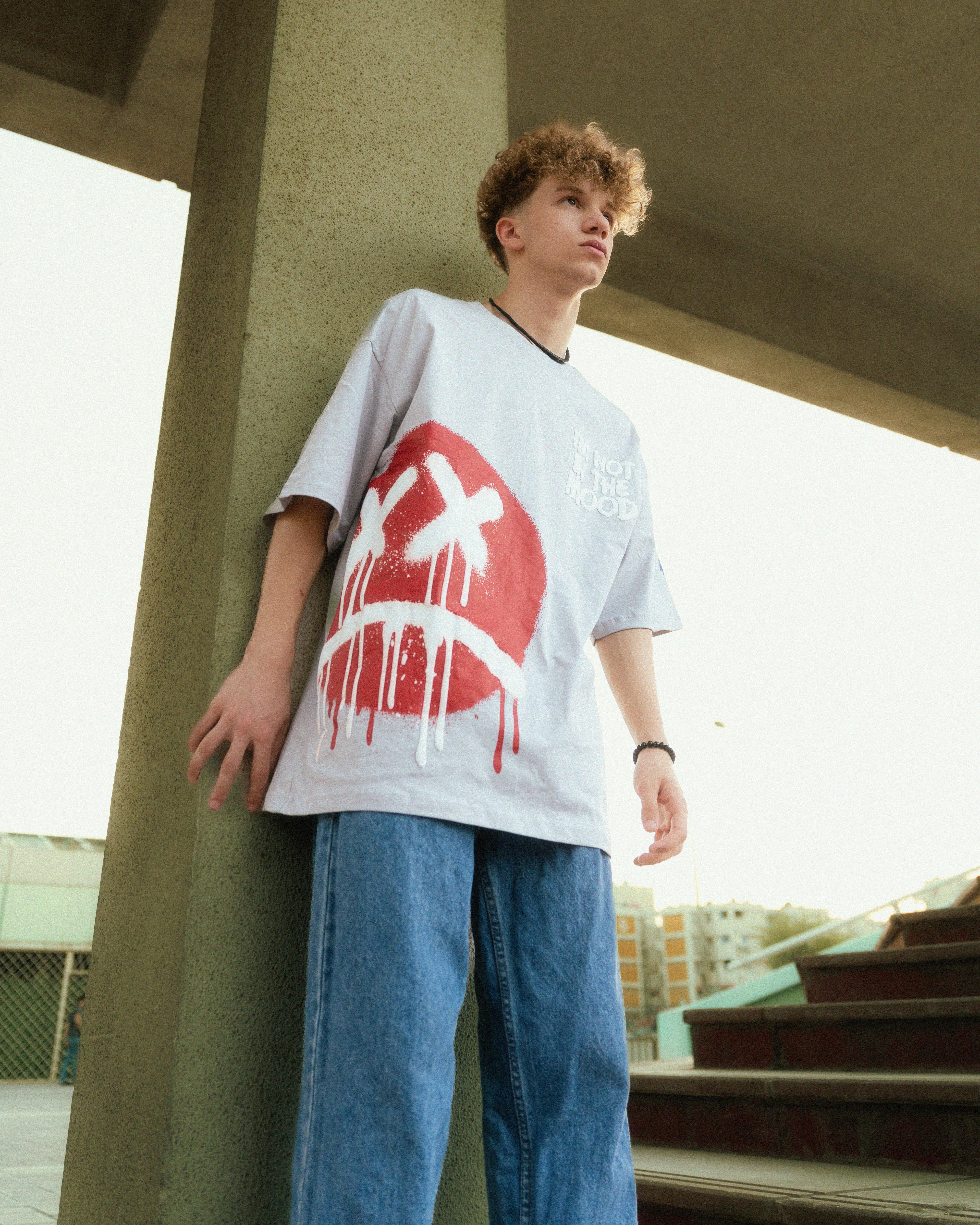 a young man standing on a concrete wall wearing a t shirt with a red cross on it