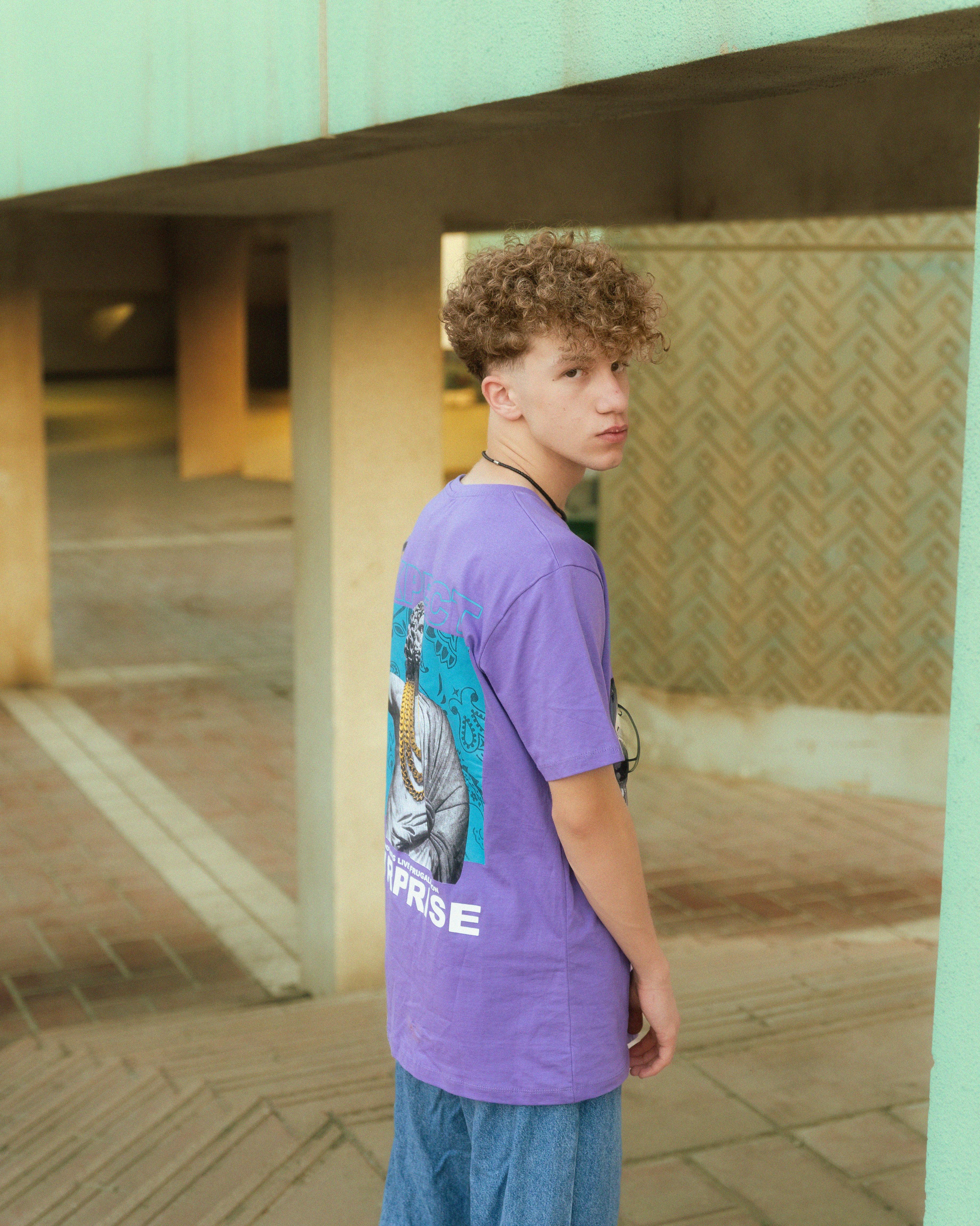 a young man in purple shirt and jeans standing in front of a building