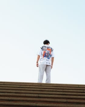 Teenager standing on steps outdoors in a graphic t-shirt, viewed from behind.