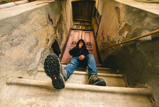 A man in casual attire sits relaxed on aged steps in an urban setting, exuding laid-back vibes.
