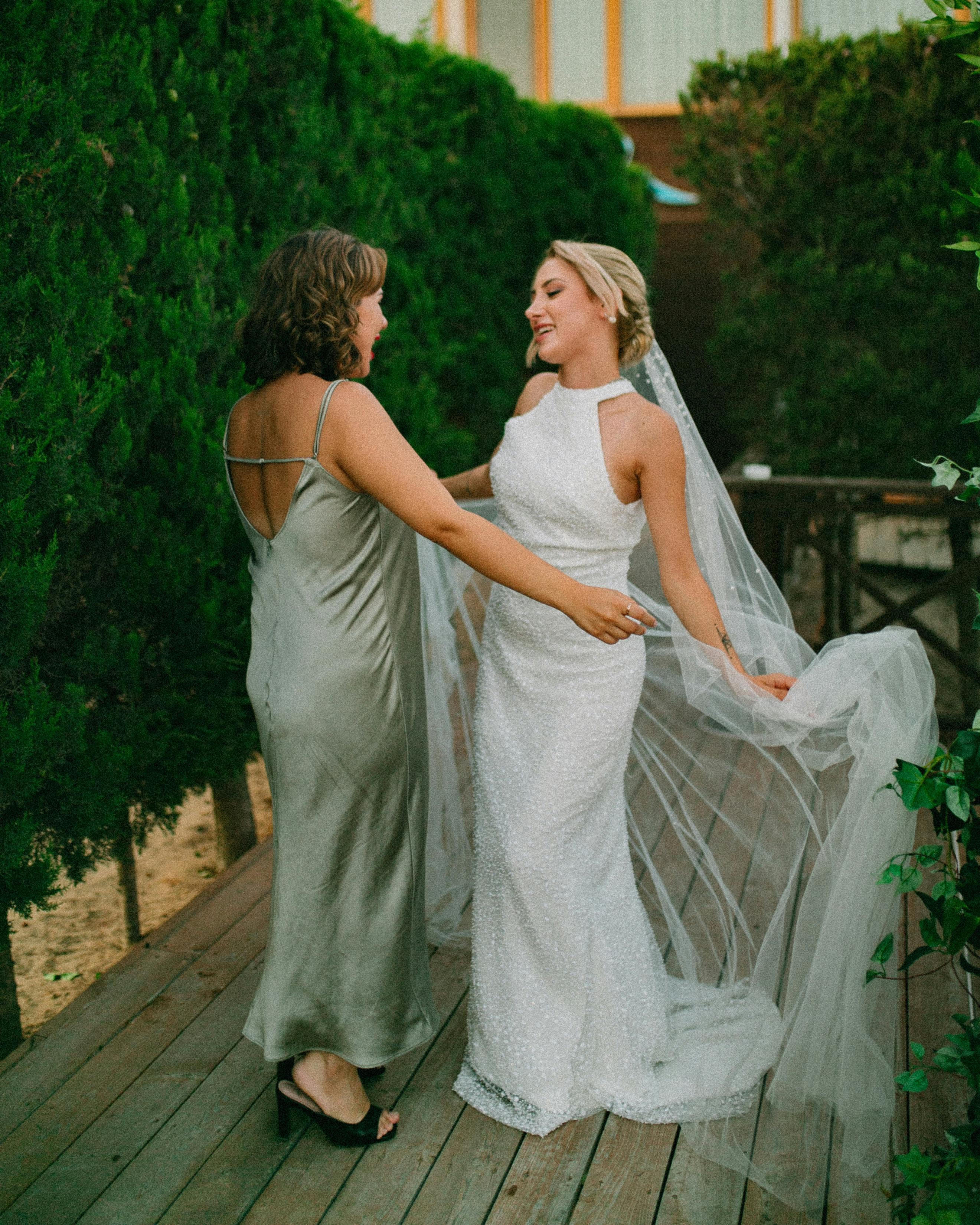 A joyful bride with her bridesmaid sharing a moment outdoors in a lush garden setting.