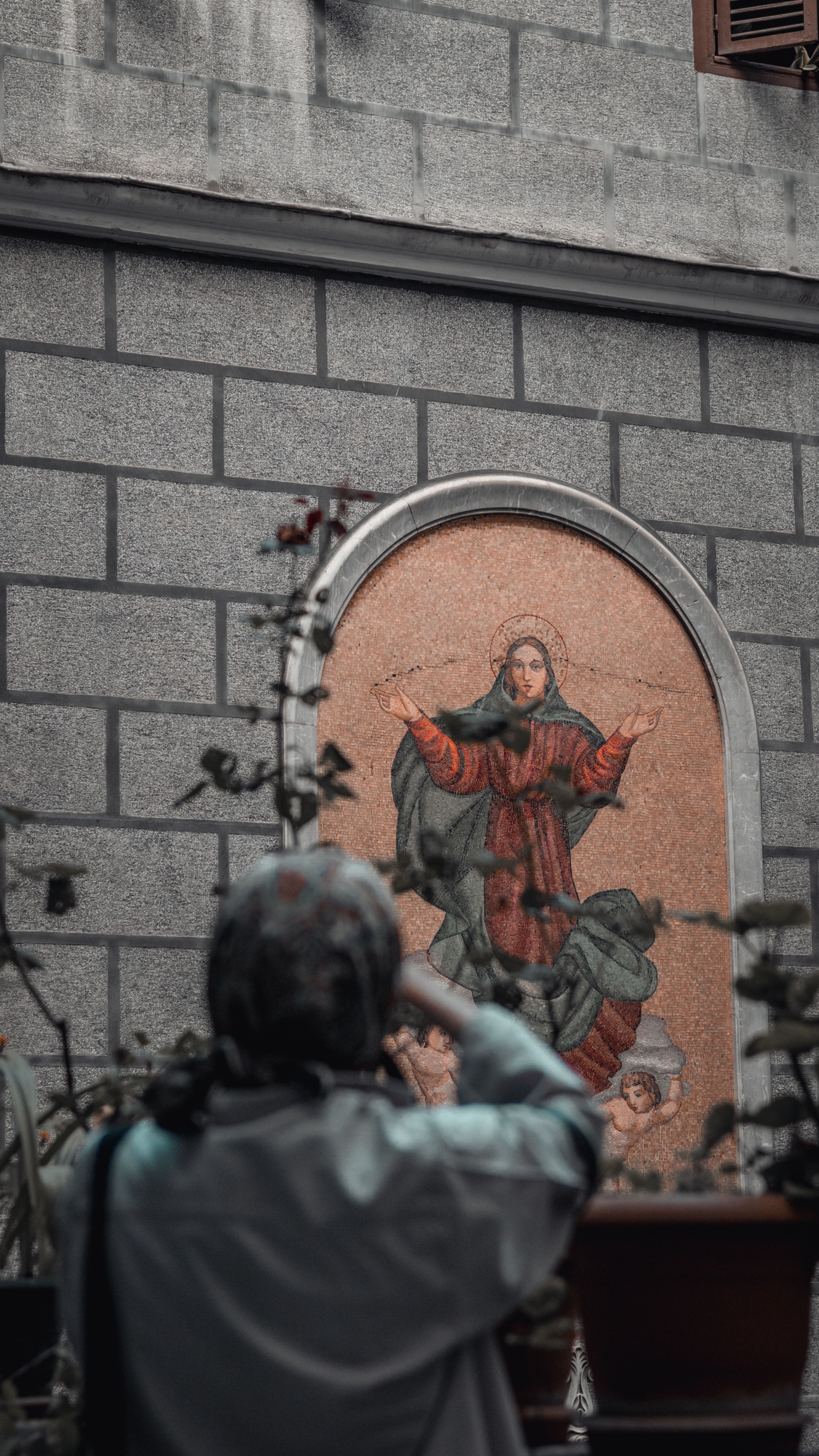 A person admires a religious mural in an urban alley, showcasing street art's cultural impact.
