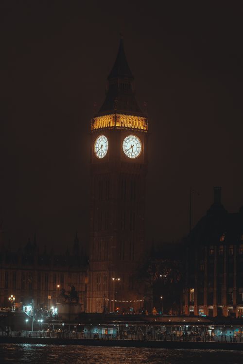 Free Illuminated night view of Big Ben tower in London, a classic architectural landmark by the Thames River. Stock Photo