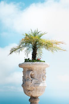 A detailed view of a decorative stone planter featuring a tropical palm tree set against a clear blue sky.
