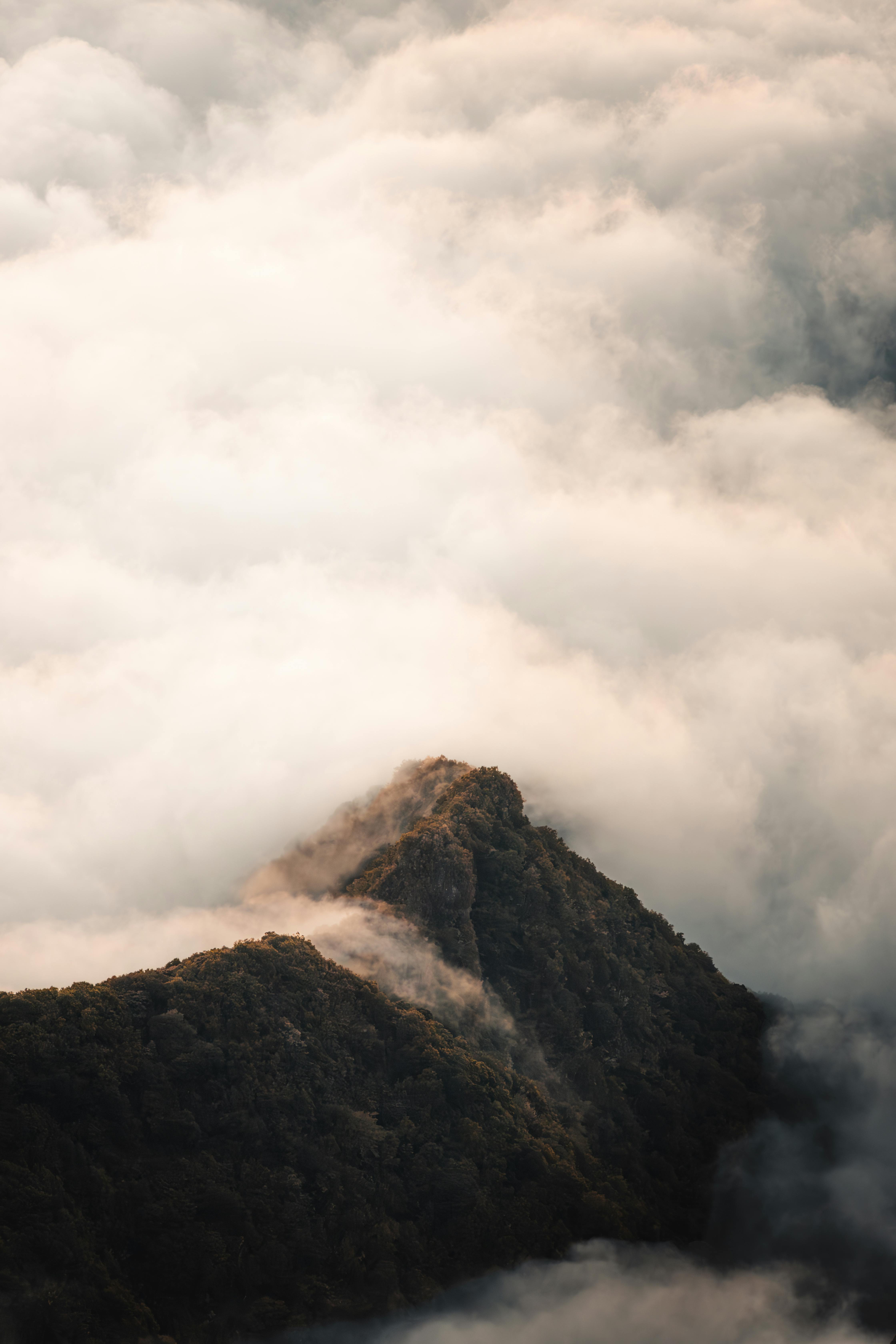 A dramatic mountain peak breaks through a thick layer of fog in Madeira, Portugal at dawn.