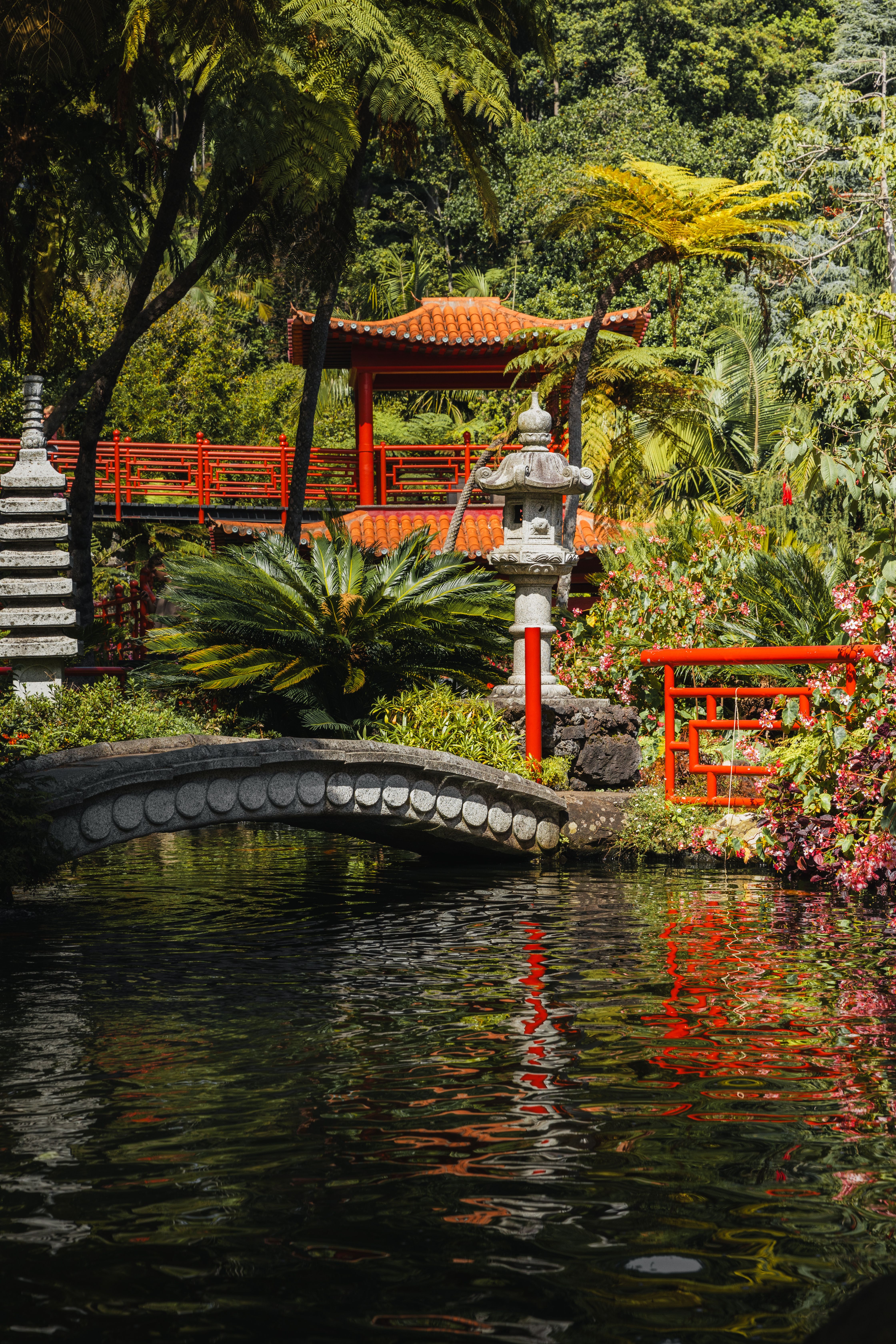 A red bridge over a pond with a garden · Free Stock Photo
