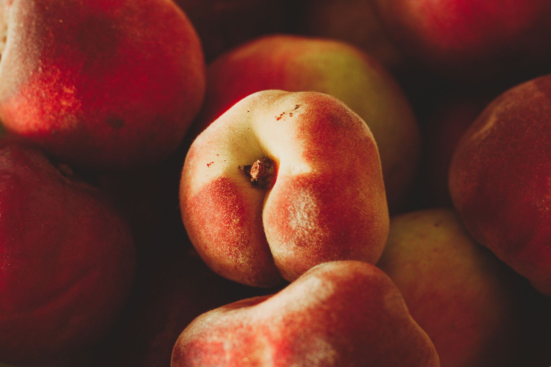 Colorful variety of fresh peaches including donut peaches on a rustic tray